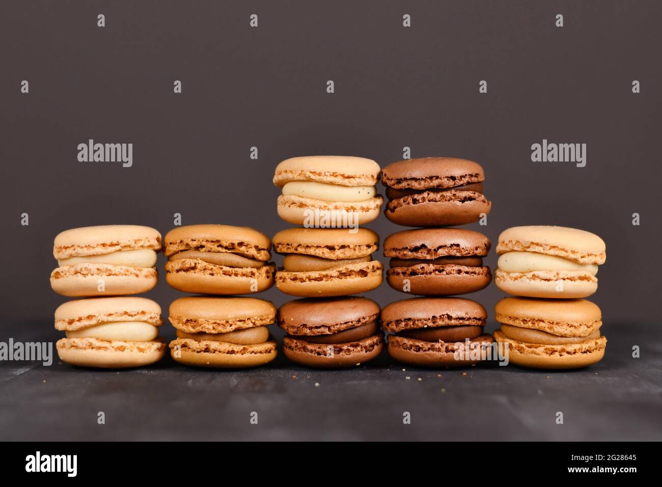 Macaron francesi di colore marrone, beige e crema accatastati davanti a sfondo scuro Foto Stock