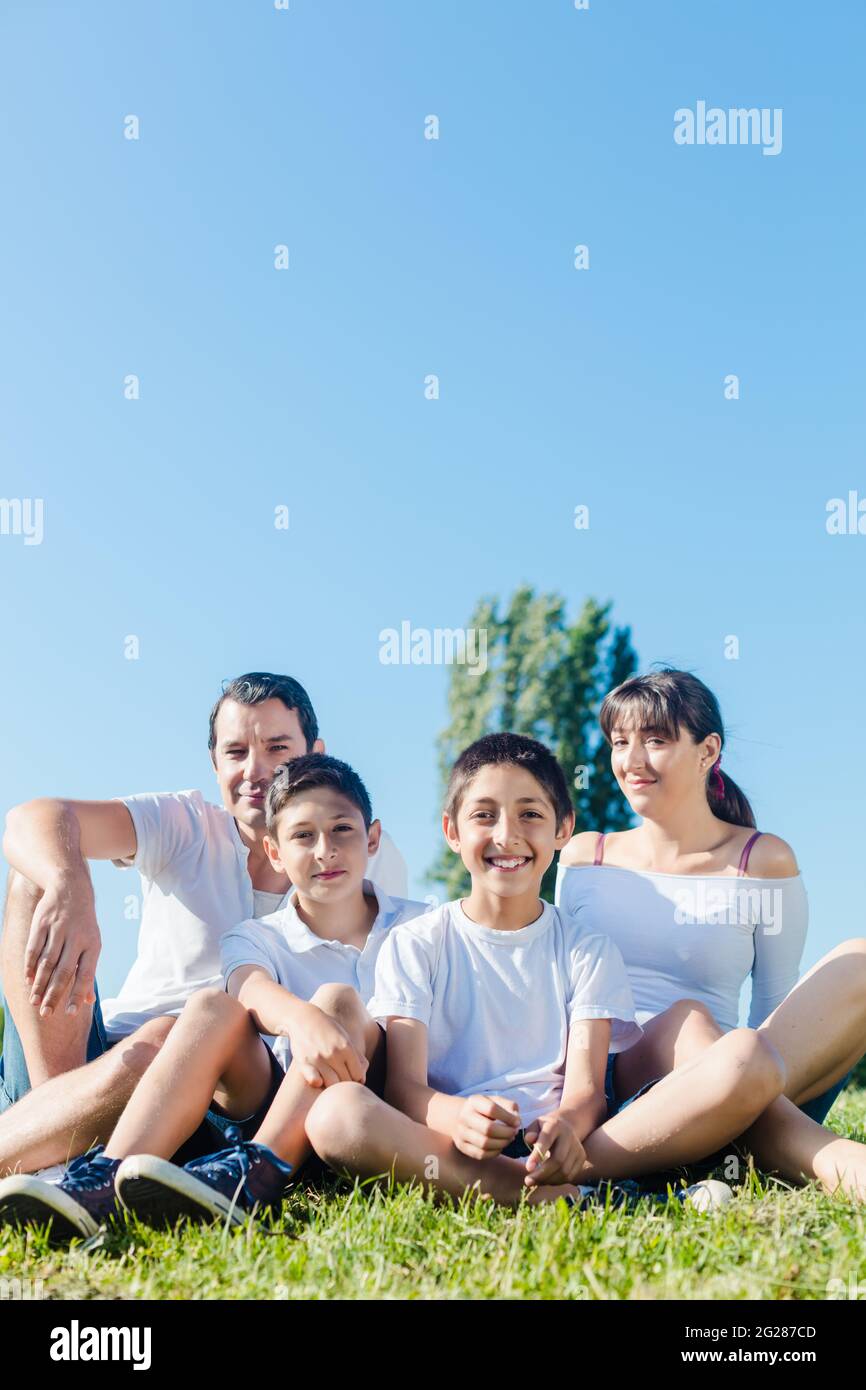 Famiglia vestita di bianco nel parco in estate seduta in Prato Foto Stock