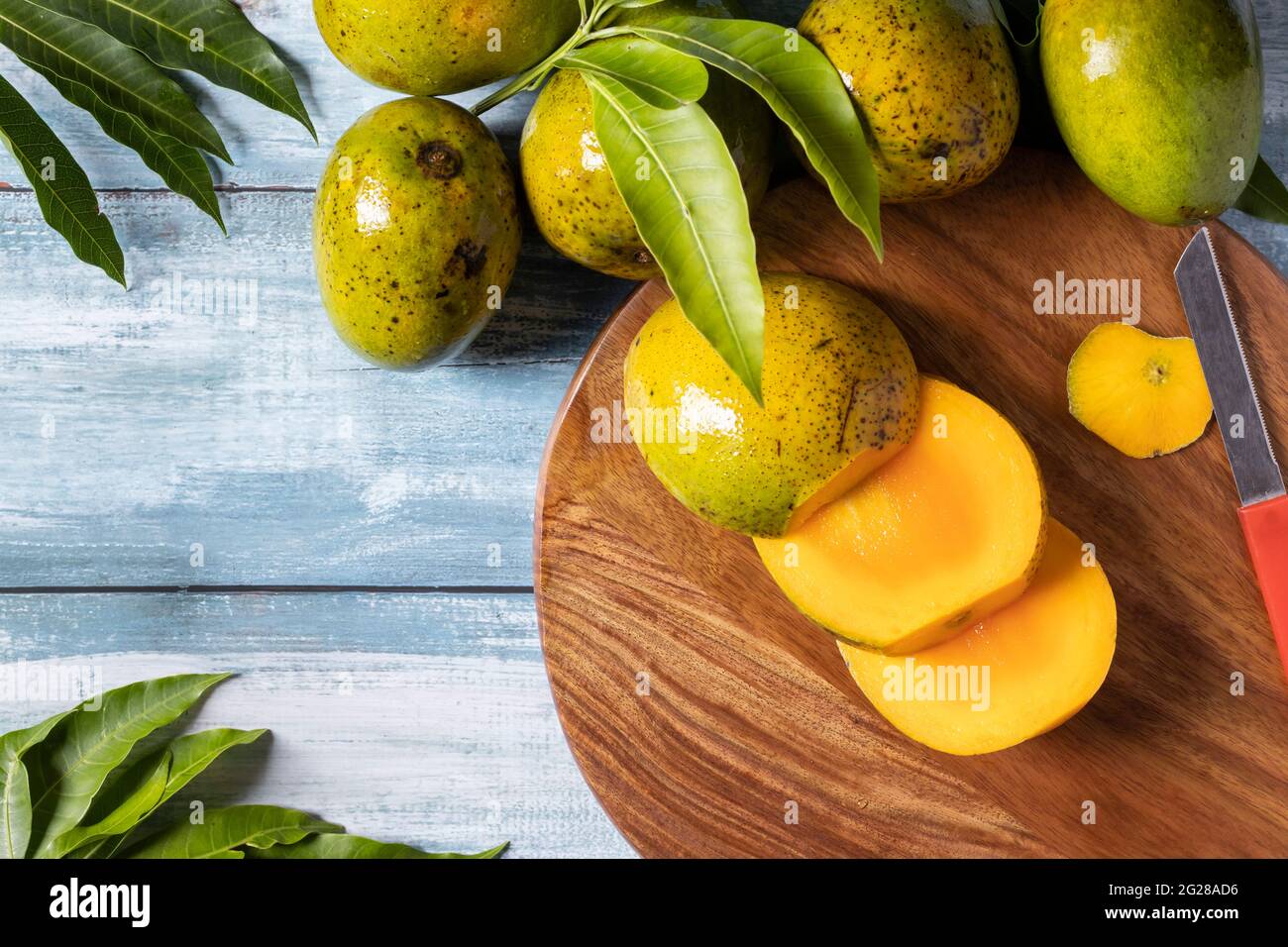 Vista dall'alto di fette di mango mature su tagliere di legno insieme a mango e foglie su un tavolo di legno Foto Stock