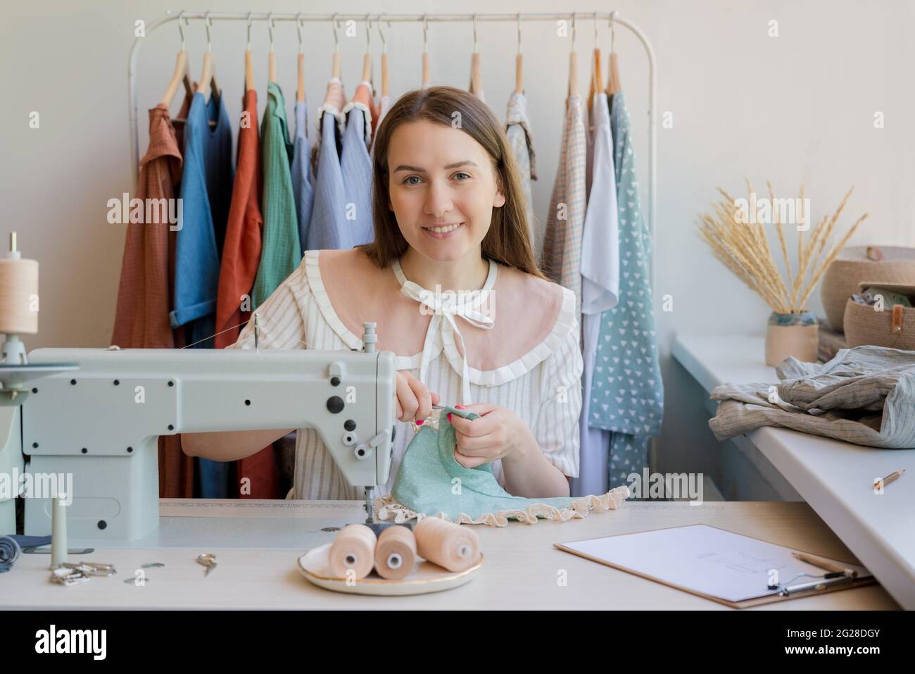 Sorridente giovane donna cucire abiti presso il suo atelier o laboratorio Foto Stock