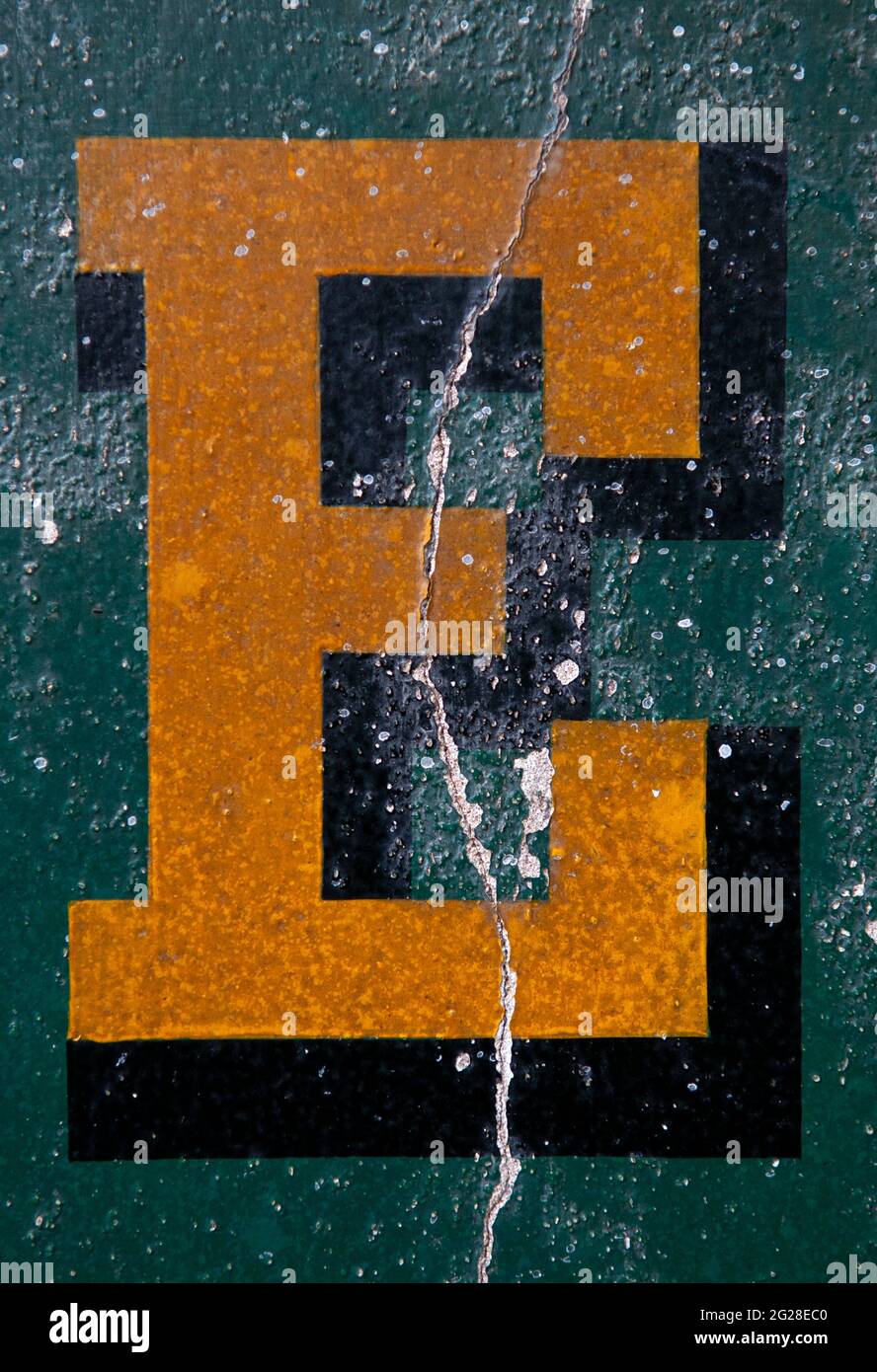 Un primo piano di UN capitale e dipinto in giallo con un ombra goccia su UNA parete verde in difficoltà e indossata Foto Stock