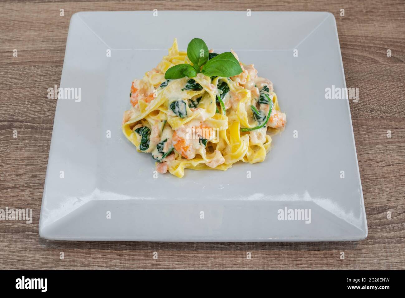 Spaghetti di pasta italiana in salsa cremosa in un piatto di ceramica, con erbe, su un tavolo testurizzato. Con gamberi, vista dall'alto Foto Stock