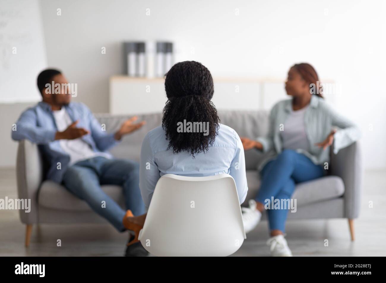 Terapia coniugale. Psicologo seduto con la schiena alla macchina fotografica durante l'appuntamento con una coppia nera infelice in ufficio Foto Stock