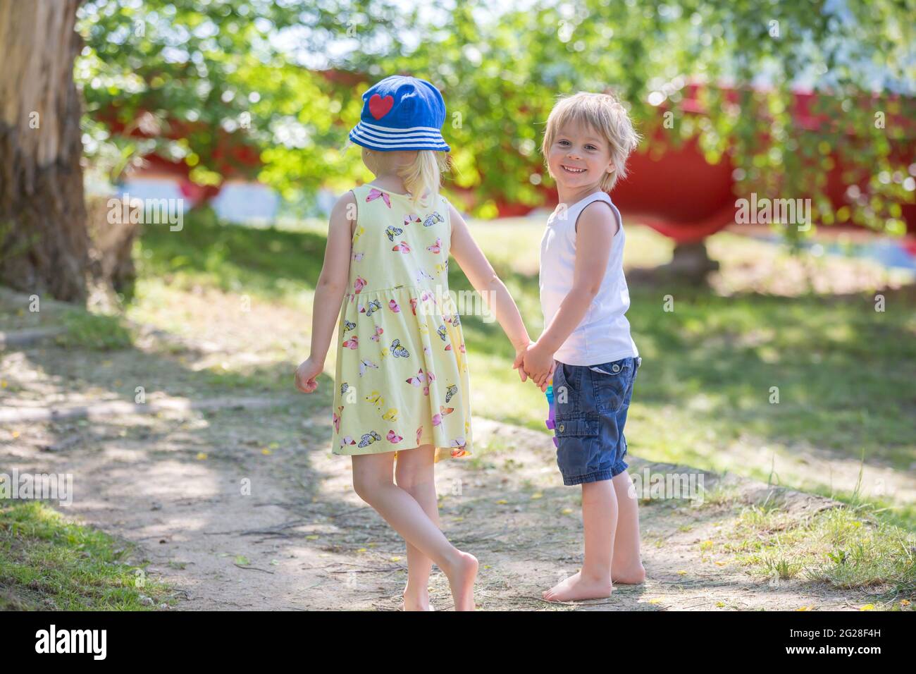 Bambini piccoli, camminando insieme a mano in mano su un piccolo sentiero accanto ad un lago con barche Foto Stock