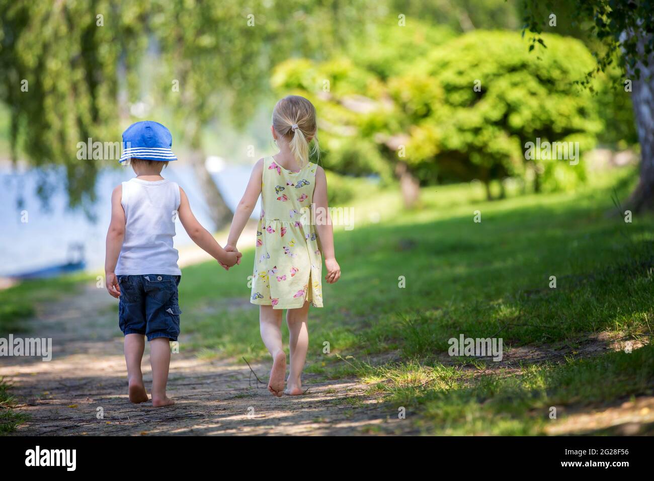 Bambini piccoli, camminando insieme a mano in mano su un piccolo sentiero accanto ad un lago con barche Foto Stock