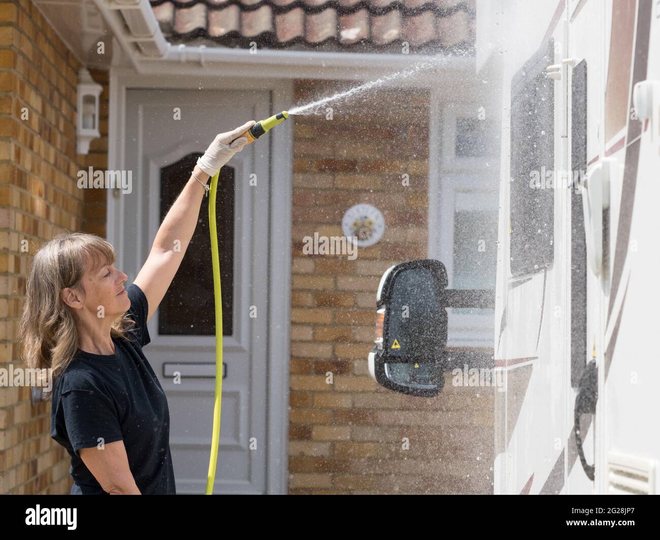Una signora proprietario del motorhome pulisce il suo veicolo ricreativo con un tubo flessibile pipe.Spray può essere visto che proviene dal tubo come signora pulisce Foto Stock