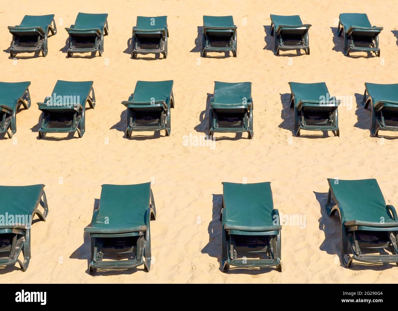 File di lettini verdi gratuiti su una spiaggia di sabbia vuota. Concetto di vacanza chiusa o bassa stagione Foto Stock