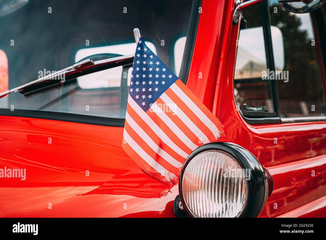 Red Pickup Truck con la bandiera americana piccola che svita. Chiudere la vista laterale di Red Pickup Truck American Flag Waving. Festa del 4 luglio. Bandiera americana che soffia Foto Stock