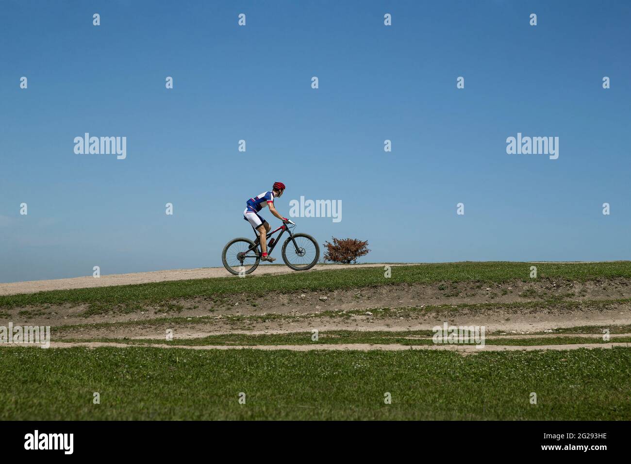 uomo in bicicletta a cavallo su una collina verde in fondo cielo blu Foto Stock