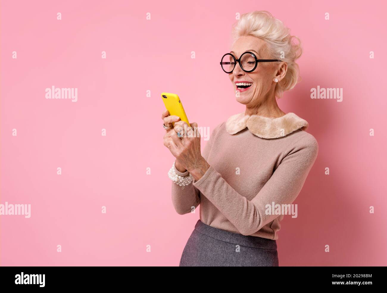La nonna usa il telefono, controlla la presenza di nuovi messaggi. Foto di donna anziana gentile su sfondo rosa. Foto Stock