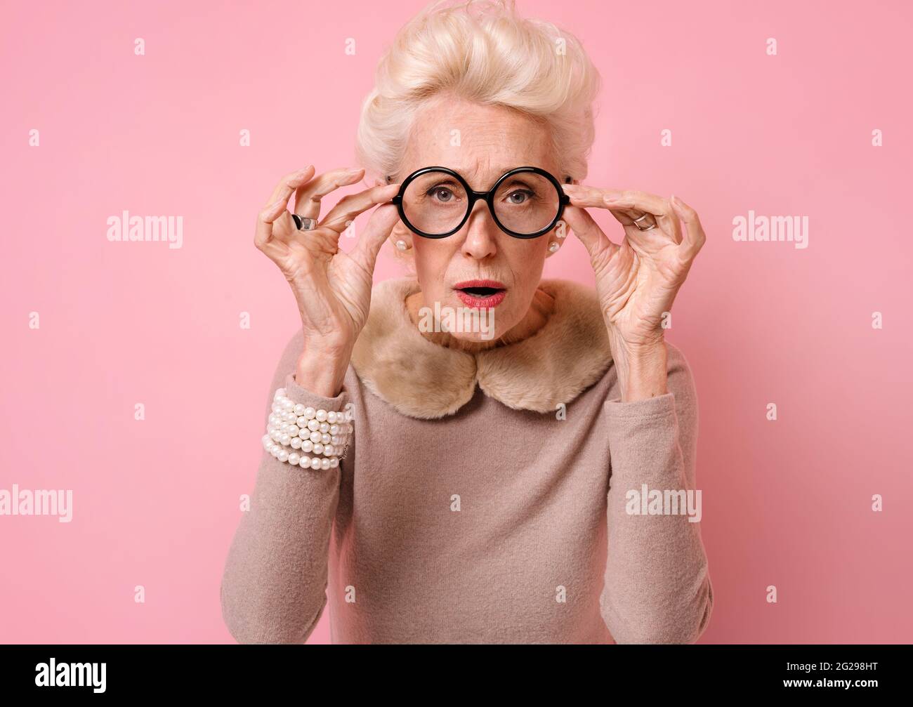Cosa, cosa? Nonna scioccata negli occhiali guardando la macchina fotografica. Foto di donna anziana gentile su sfondo rosa. Foto Stock