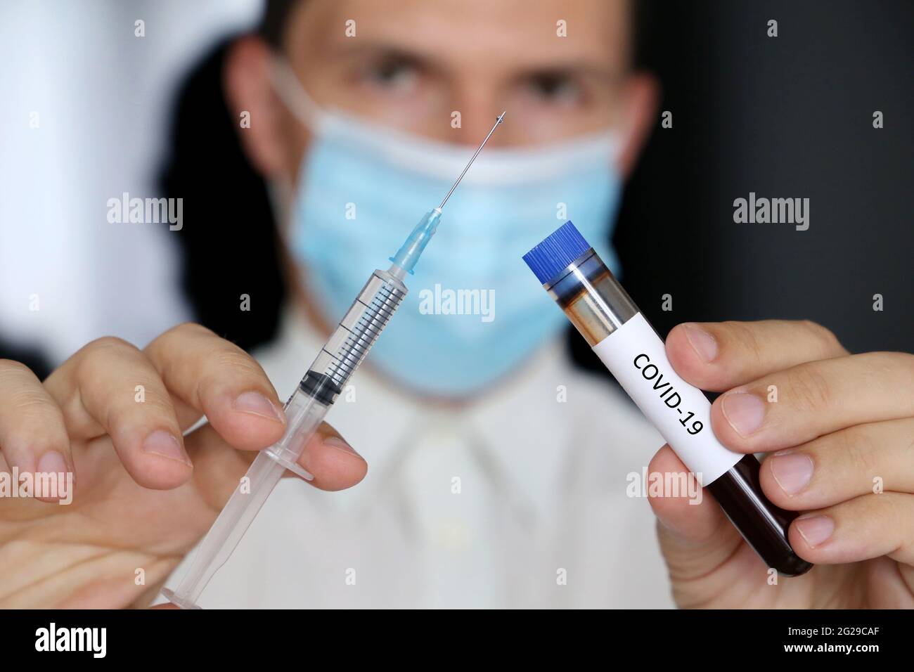 Medico in maschera con siringa e campione di sangue di covid-19 in provetta in mani. Concetto di vaccinazione e test medici Foto Stock