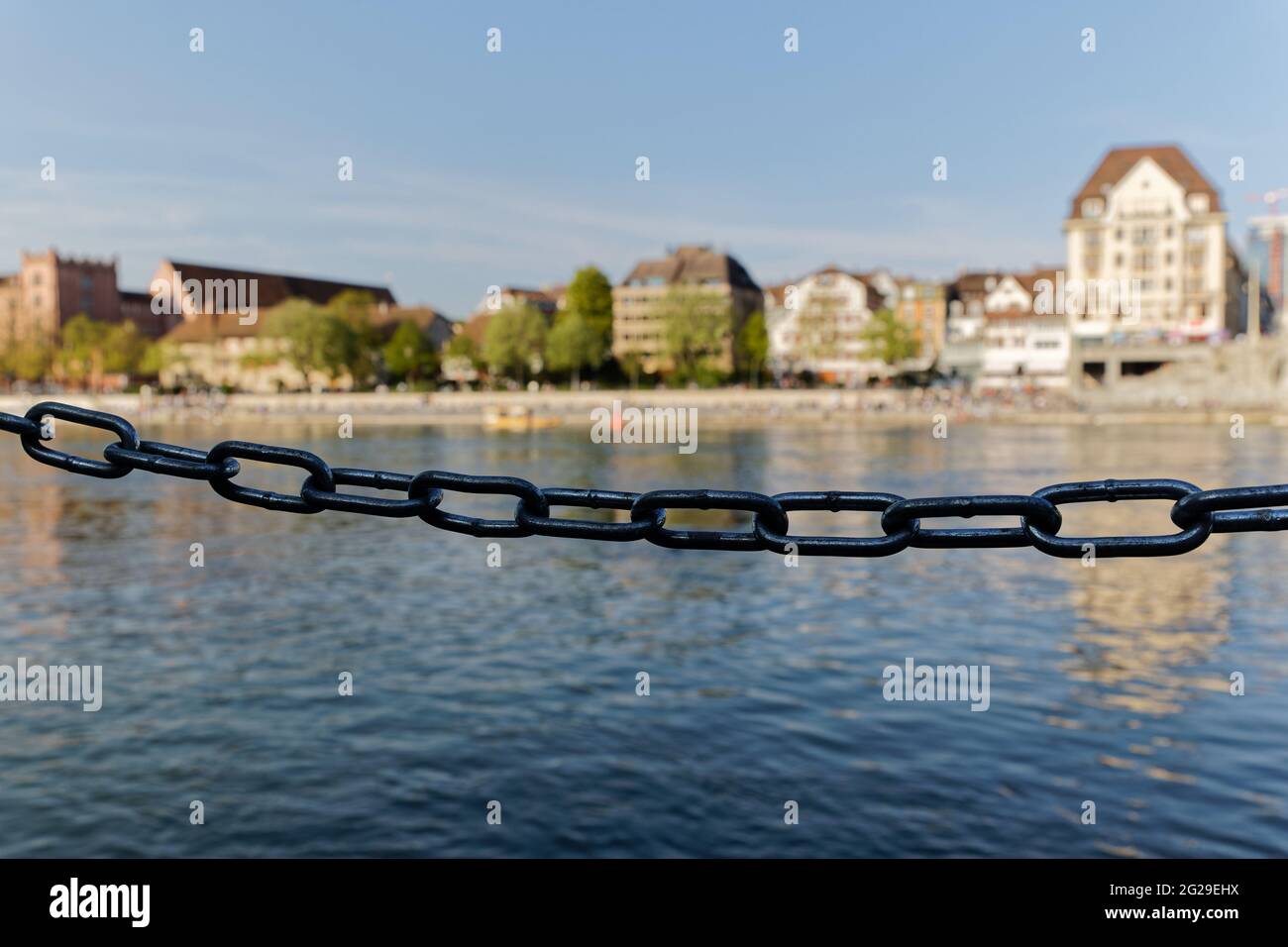 catena di metallo barriera in ombra di fronte al fiume blu e la facciata della casa, forte fuoco sulla catena di metallo, sfondo sfocato, nel sole di giorno Foto Stock