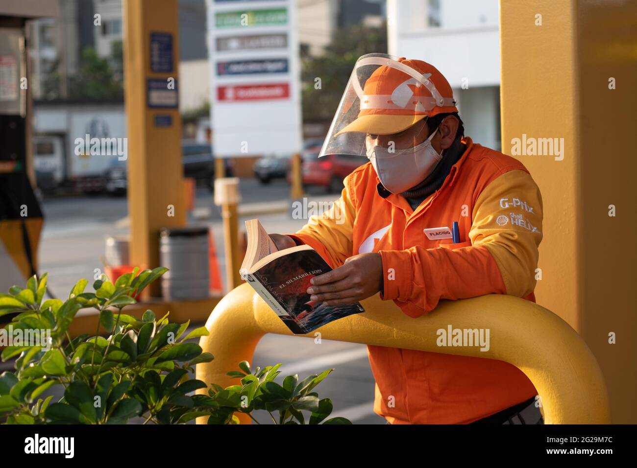 Giovane operaio peruviano che indossa un'uniforme arancione e una maschera  Covid legge il libro di Silmarillion nella stazione di benzina Primax dove  lavora a Lima Foto stock - Alamy
