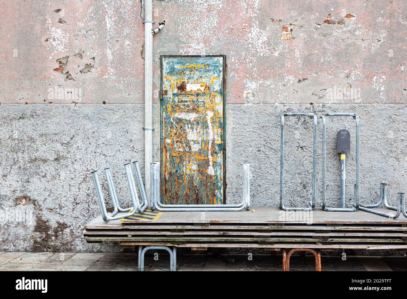 Diversi bacini alluvionali sono accatastati di fronte a un muro di mattoni in sfumature pastello e una porta in metallo arrugginita e dipinta brillantemente Foto Stock