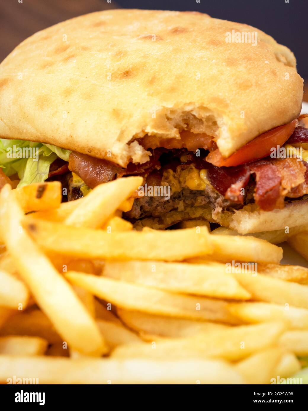 Un partrone ha preso un morso da un cheeseburger di pancetta guarnito con  pomodoro e lattuga. Le patatine fritte sono sfocate in primo piano Foto  stock - Alamy