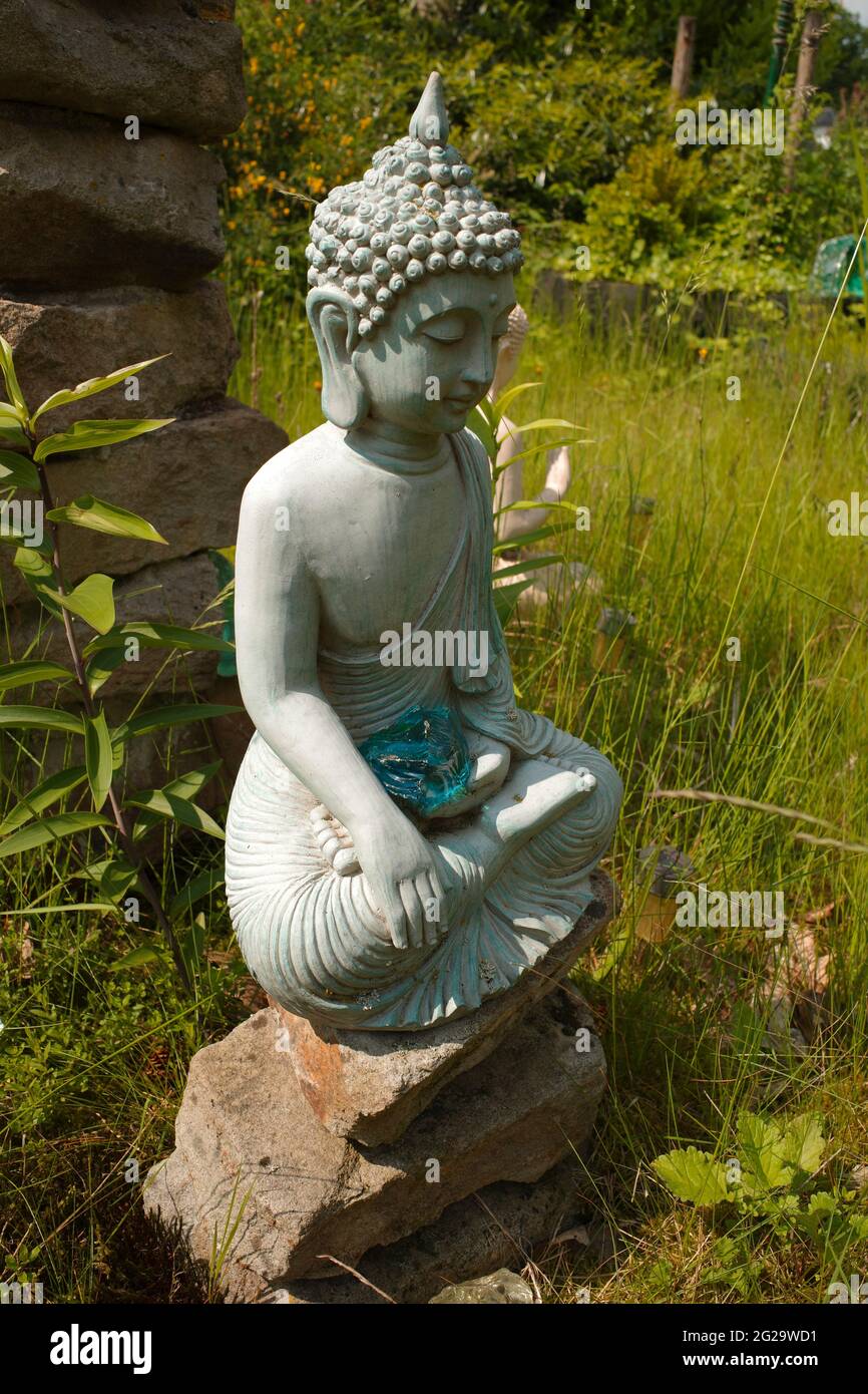 buddha grigio-blu seduto su un mucchio di pietre. Ha una pietra di vetro turchese sul suo grembo. Il suo gesto della mano si chiama Bhumisparsha Mudra . Foto Stock