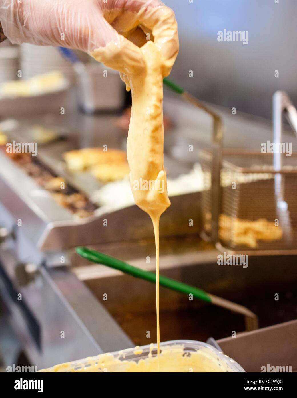 Uno chef immerge un pezzo di pesce in pastella prima di cuocere il pesce in una friggitrice a olio caldo. Foto Stock