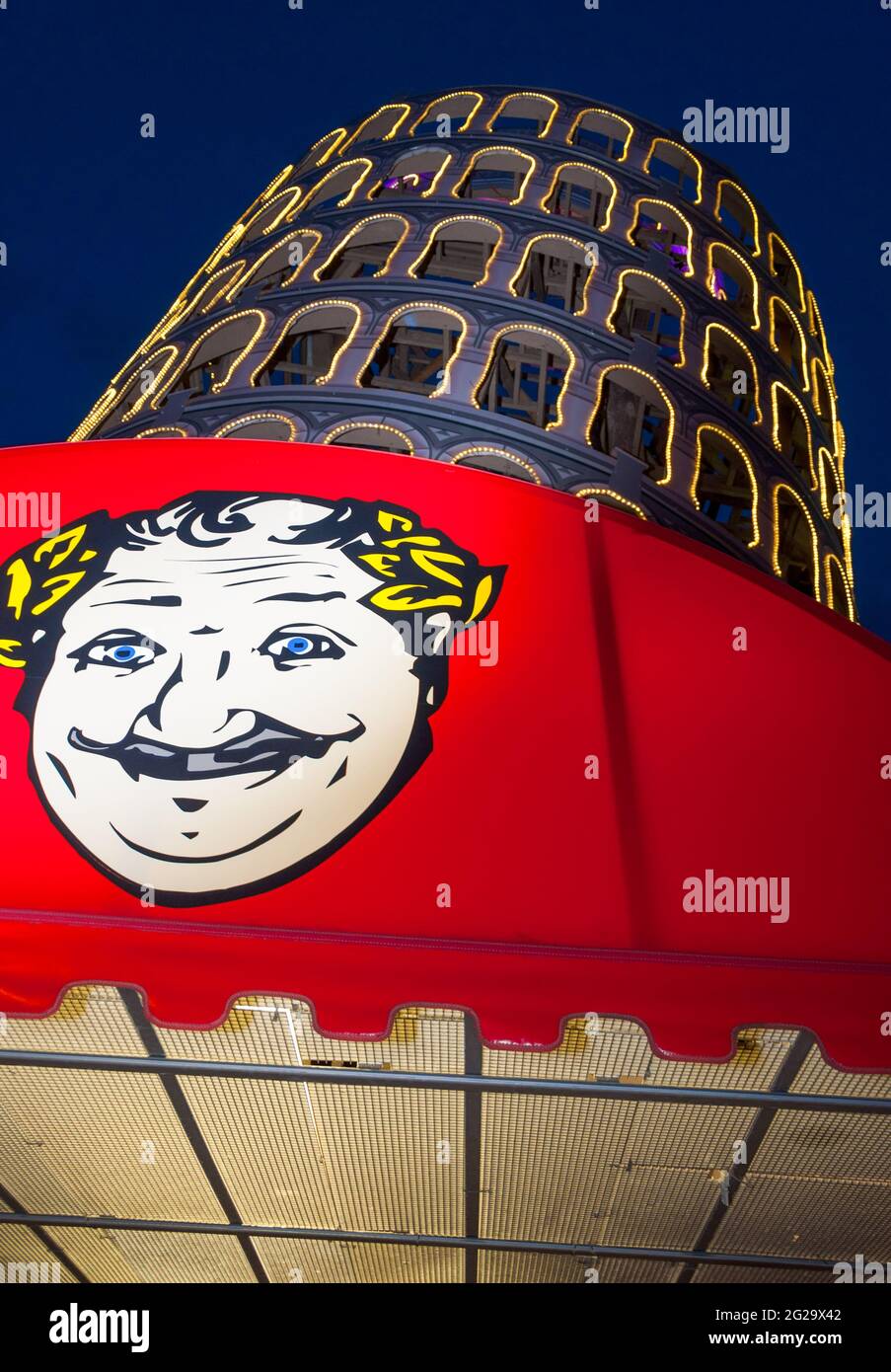 La replica della Torre Pendente di Pisa si fa balzare dietro un baldacchino rosso che presenta un disegno di un uomo sorridente che ha occhi blu, baffi e allori intorno a lui Foto Stock