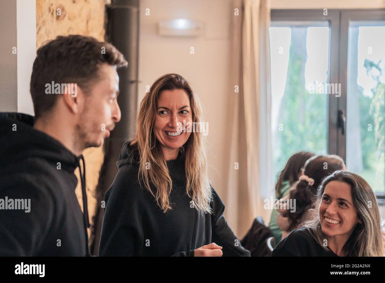Allegre donne dai capelli lunghi che guardano all'uomo e parlano con il gruppo in una stanza luminosa Foto Stock