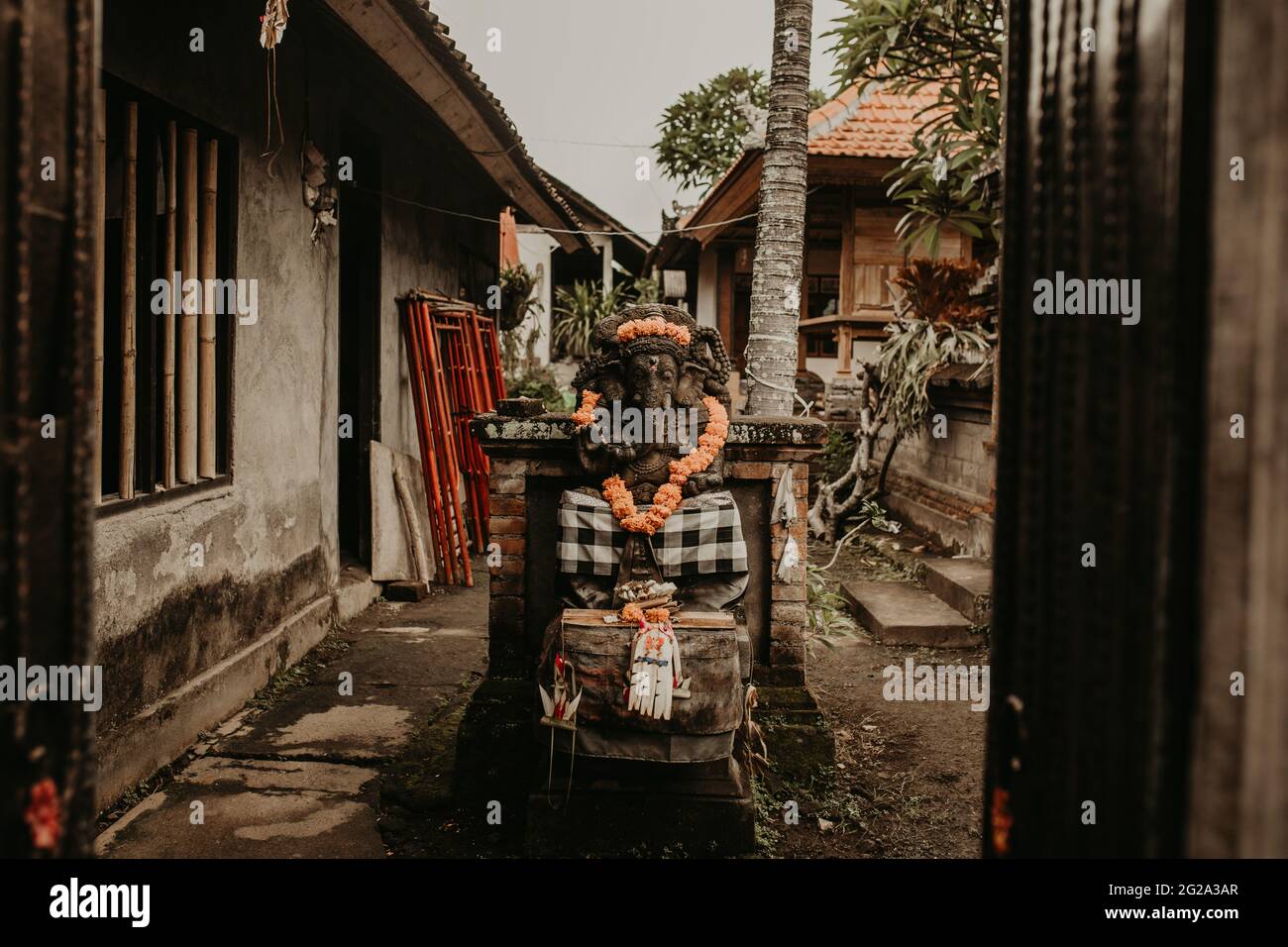 Piccolo idolo religioso tradizionale decorato con fiori collocato su un tranquillo cortile esotico Foto Stock