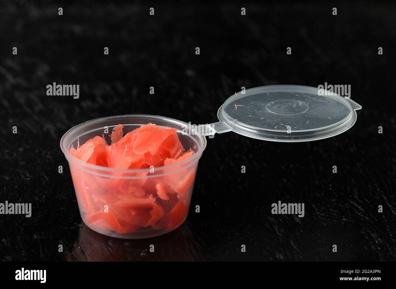 Radice di zenzero tagliata a fette sottili di colore rosso in un vaso di plastica di consegna. Messa a fuoco selettiva. Foto Stock