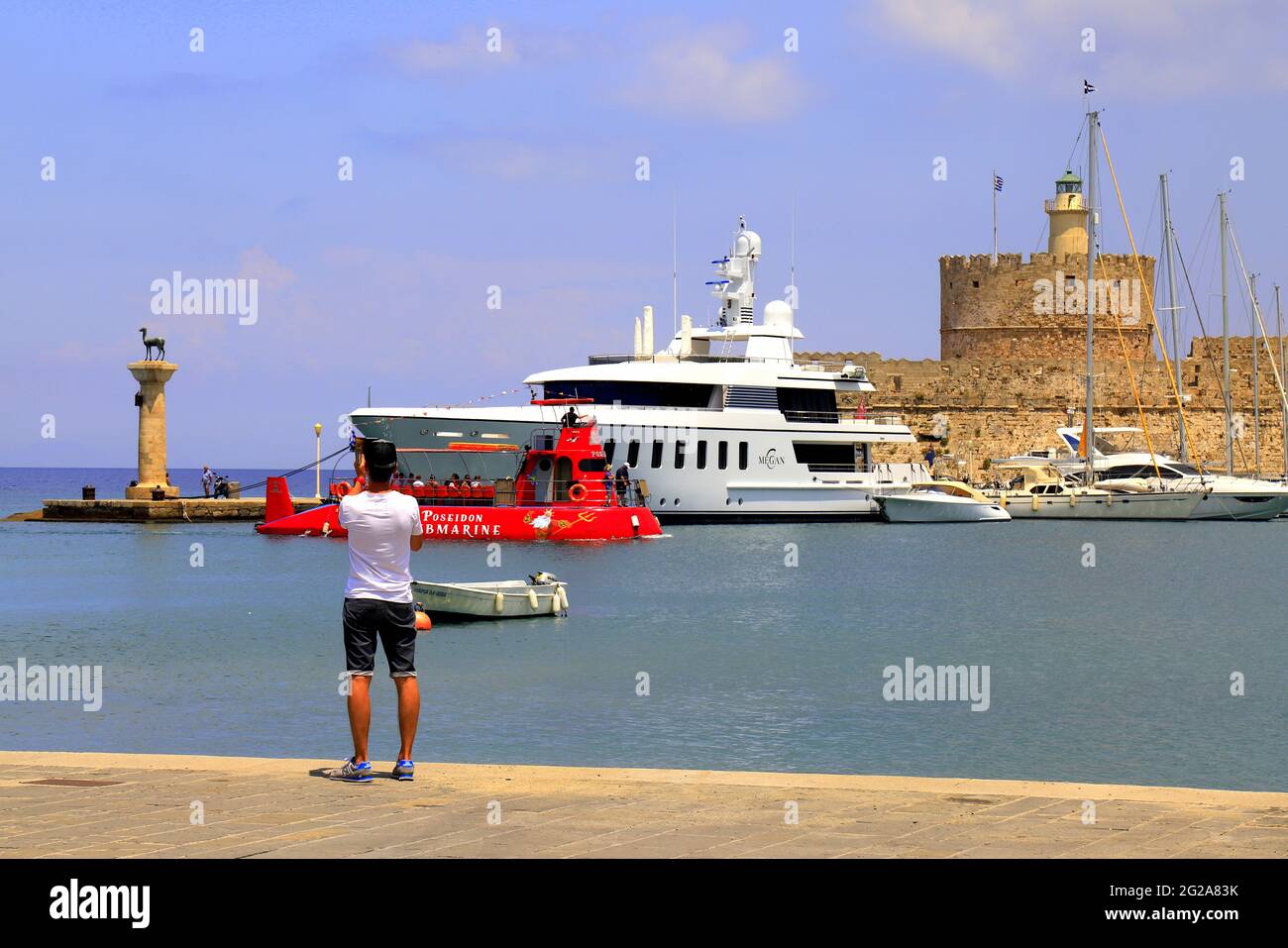 I turisti nel porto di Rodi scattano foto di sottomarino rosso, yacht e fortezza medievale. Vacanza estiva al mare, luogo bellissimo per viaggi e relax Foto Stock