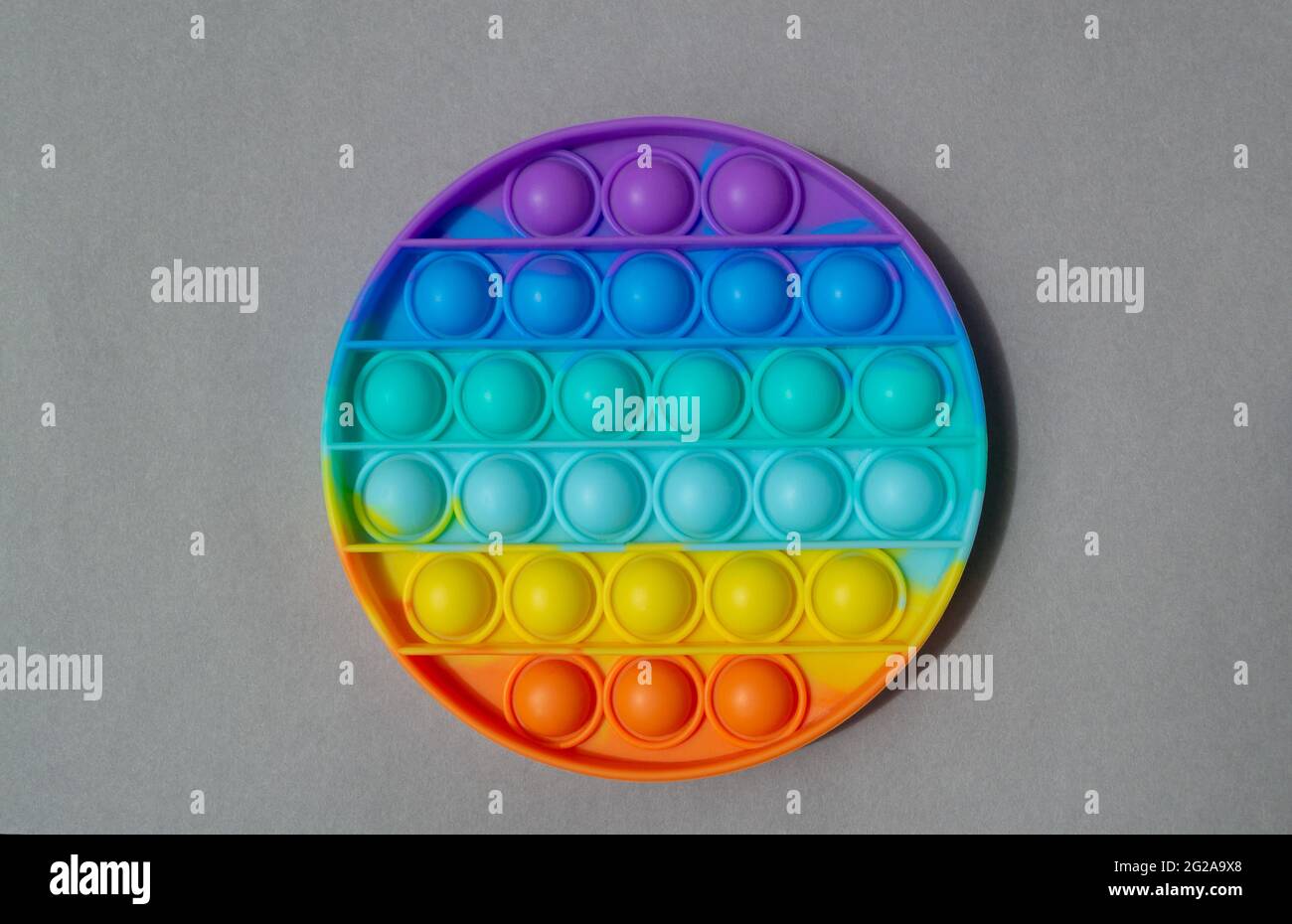 Giocattolo in silicone colorato e luminoso Pop IT. Popolare giocattolo anti stress su sfondo grigio Foto Stock