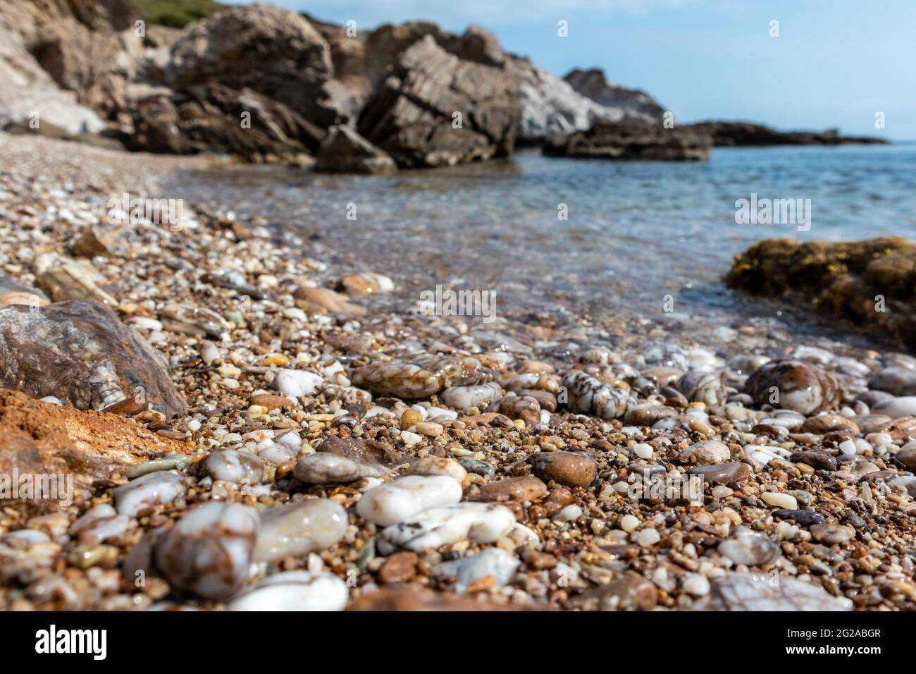 Pietre di marmo da vicino sulla spiaggia di ghiaia del Mar mediterraneo selvaggio con scogliere rocciose e acque blu chiare. Viaggia in Grecia vicino ad Atene. Estate natura s Foto Stock