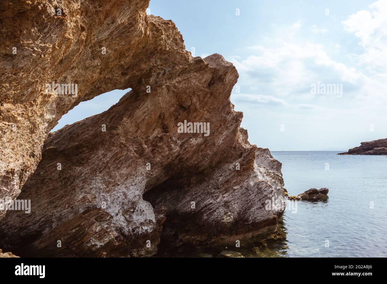 Grande roccia con un buco vicino vista sulla spiaggia selvaggia del mediterraneo con acqua cristallina. Viaggia in Grecia vicino ad Atene. Estate natura laguna panoramica Foto Stock