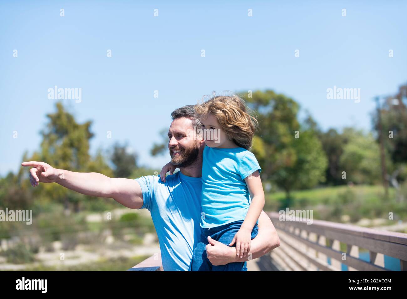 Felice padre uomo tenere figlio bambino in armi che punta dito estate all'aperto, parenting Foto Stock