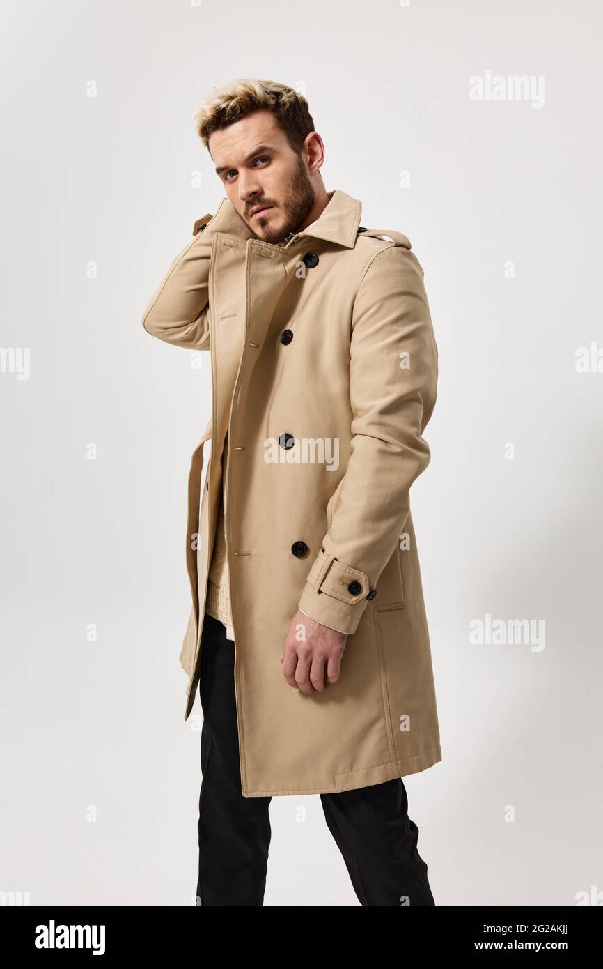 un uomo biondo con un cappotto beige e pantaloni scuri che guardano in  avanti su uno sfondo chiaro Foto stock - Alamy