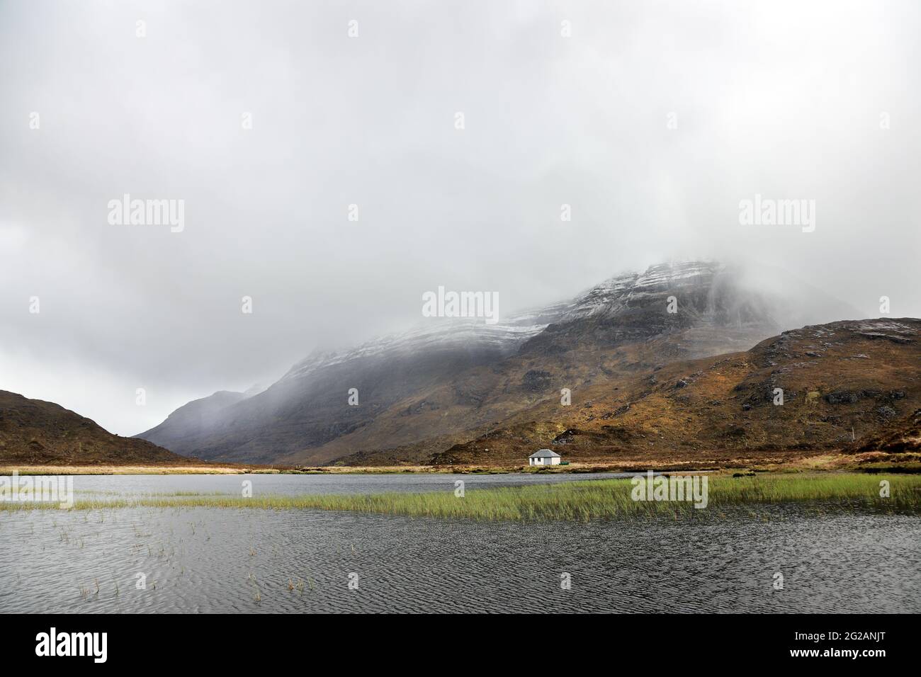 La montagna di Liathach si avvolse nella nuvola mentre Snow Shower scorre sui suoi fianchi, visto attraverso Lochan An Lasgair, Torridon, Scozia, Regno Unito Foto Stock
