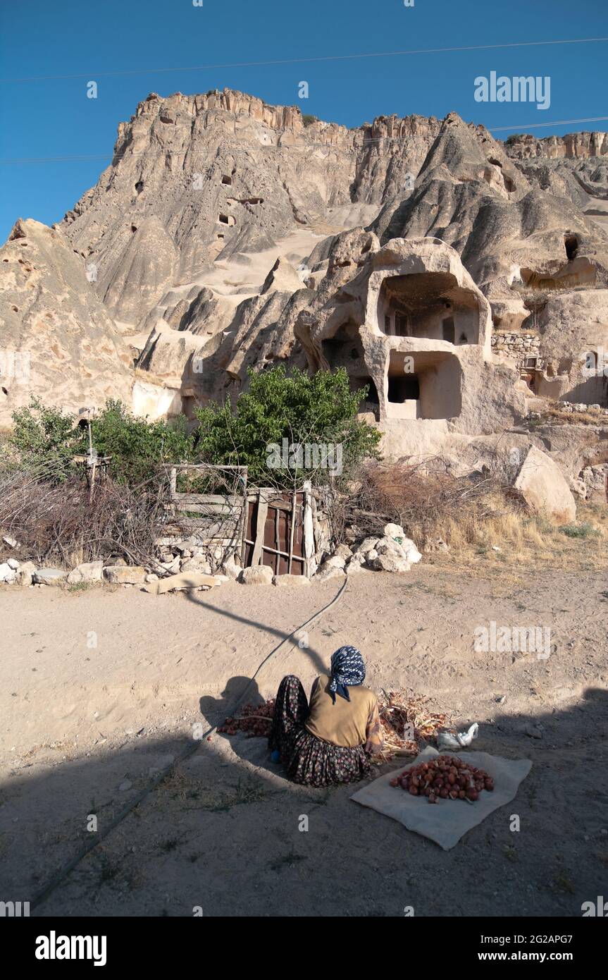 Yaprakhisar, Turchia - 31 luglio 2010: Una donna musulmana anziana pulisce le cipolle che si trovano di fronte alle montagne con molte grotte scavate Foto Stock