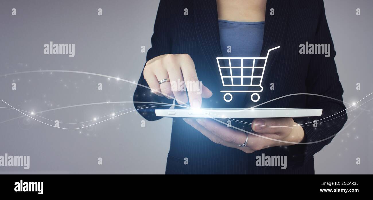 Tavoletta bianca in mano di donna d'affari con ologramma digitale Carrello icona segno su sfondo grigio. Marketing digitale online Foto Stock