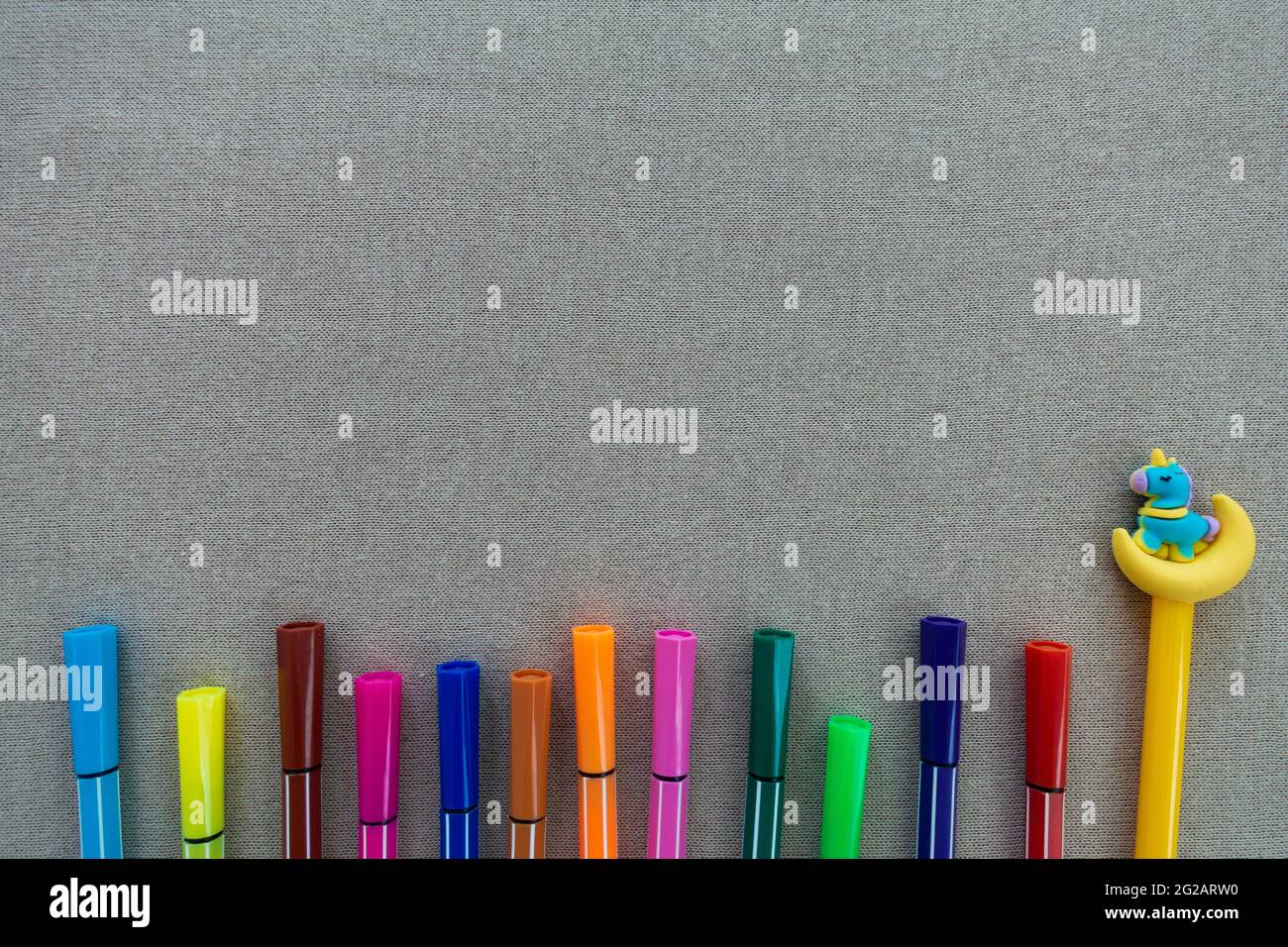 Penna a colori in molti colori, un giallo con un unicorno blu sulla parte superiore, su sfondo beige o grigio spazio copia. Foto Stock