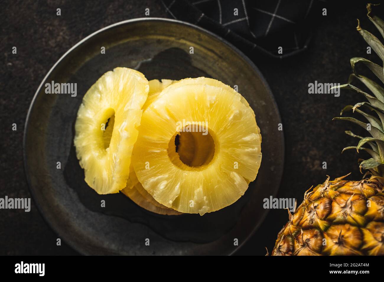 Frutta di ananas in scatola a fette su piatto su tavola nera. Vista dall'alto. Foto Stock