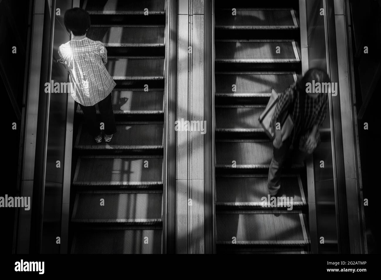Una donna si trova pazientemente su un lato di una scala mobile, mentre un'altra donna corre sull'altro lato presso una stazione ferroviaria a Yokosuka, Giappone. Foto Stock