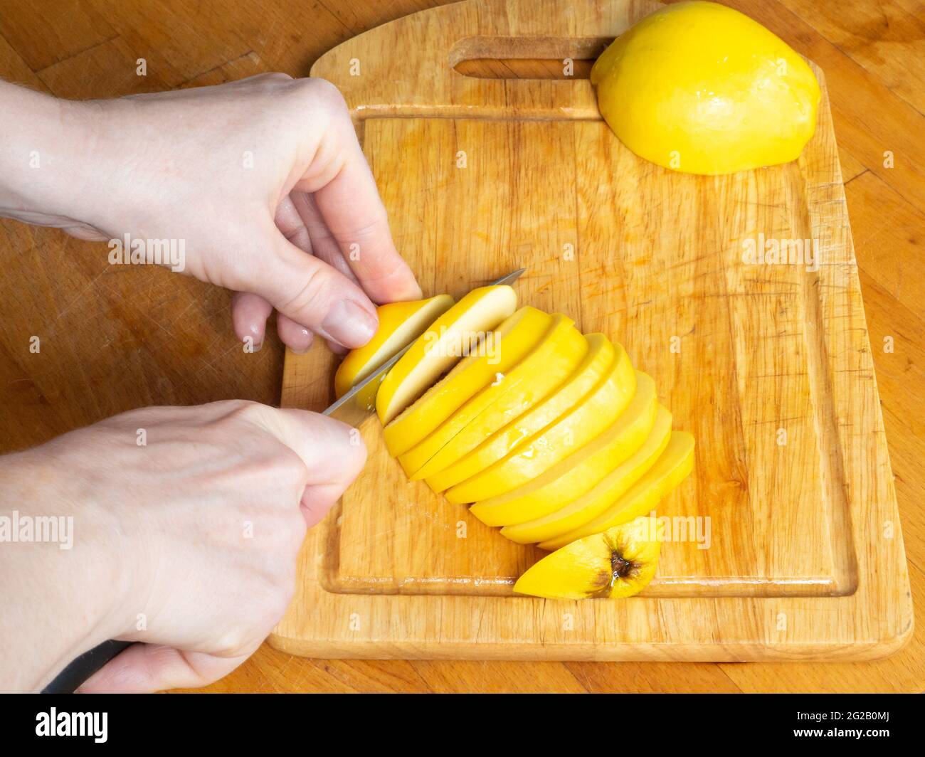 Mani tagliate con un coltello affilato giallo IVA in pezzi sottili su una tavola di legno da cucina. Foto Stock
