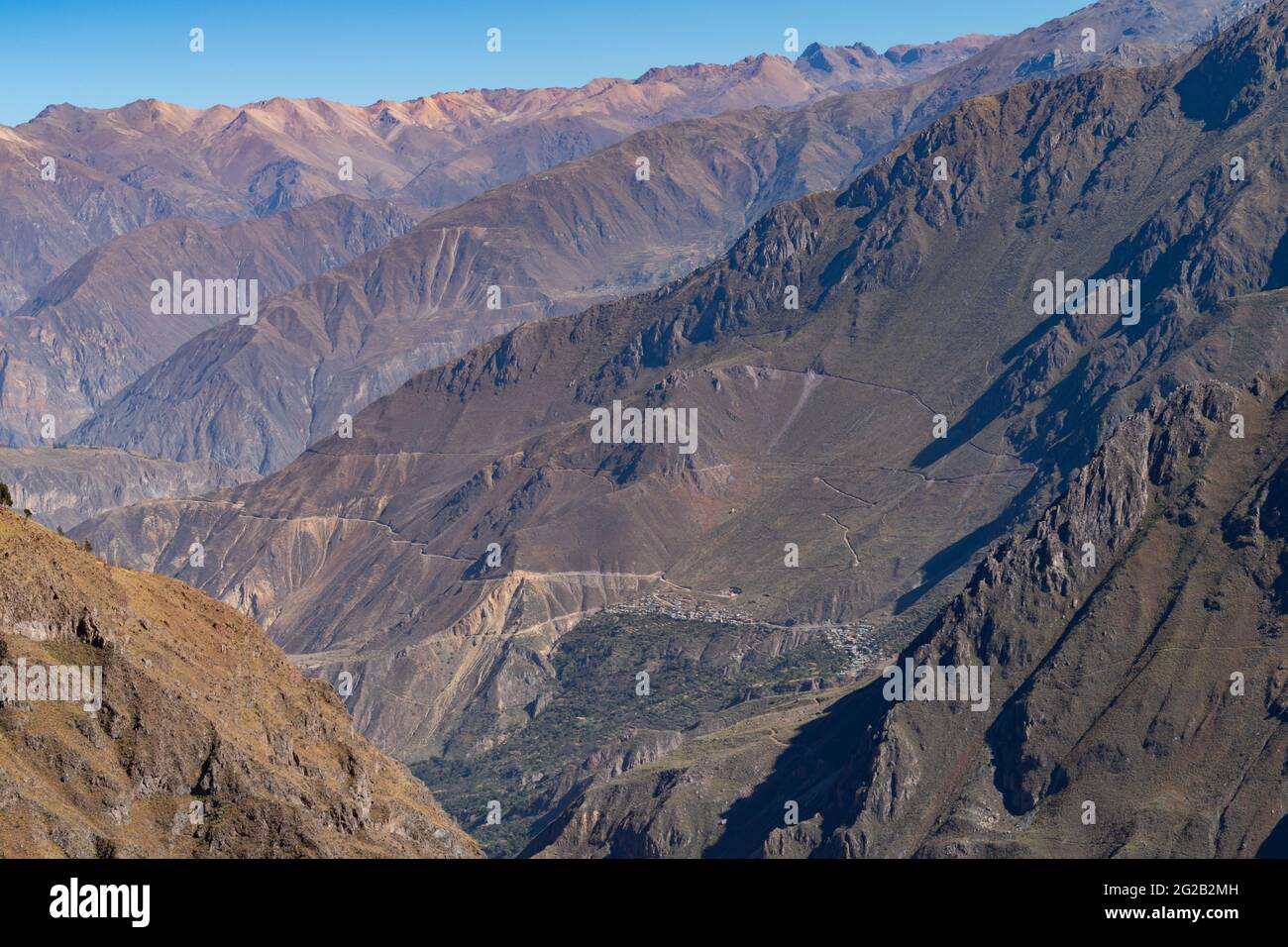 Vista panoramica del Colca Canyon, Perù, con sentieri escursionistici e un villaggio in riva alla scogliera visibile in lontananza Foto Stock