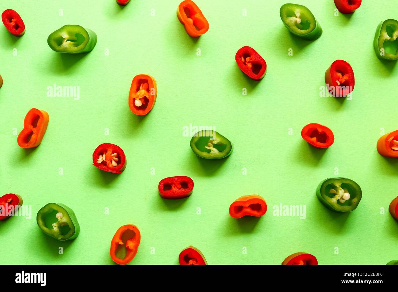 Chili a fette multicolore su sfondo verde, concetto di minimalismo creativo con spazio di copia. Vista dall'alto. Foto Stock