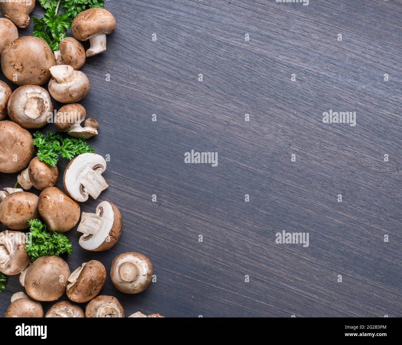 Funghi commestibili di colore marrone o funghi cremini su tavola nera con erbe. Vista dall'alto. Foto Stock
