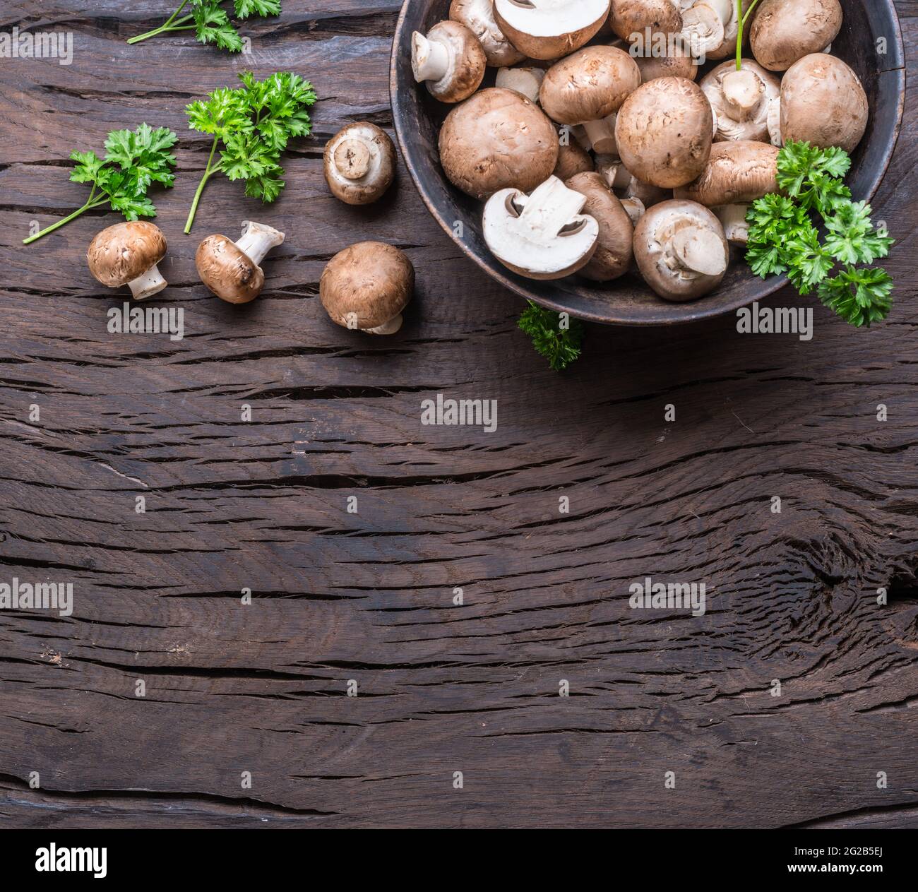 Funghi comuni di colore marrone su tavola di legno con erbe. Vista dall'alto. Foto Stock