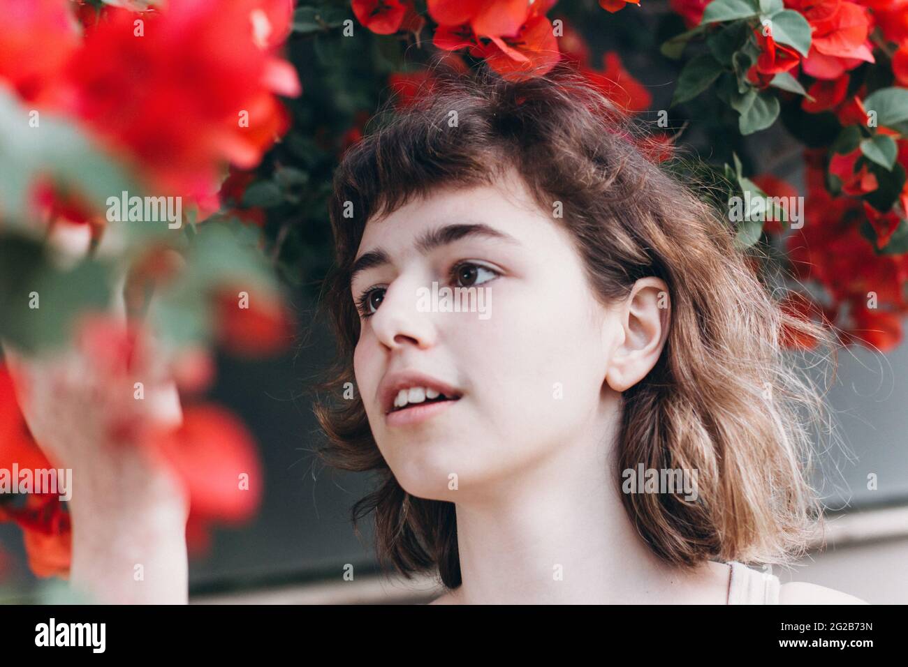 Giovane ragazza con fiori rossi. Profumo e cosmetici biologici Foto Stock