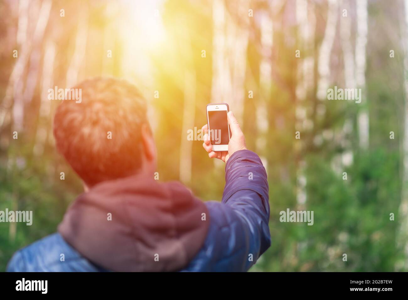 Un uomo con il suo smartphone cellulare alla ricerca del segnale di ricezione nella foresta primaverile soleggiata. Foto Stock
