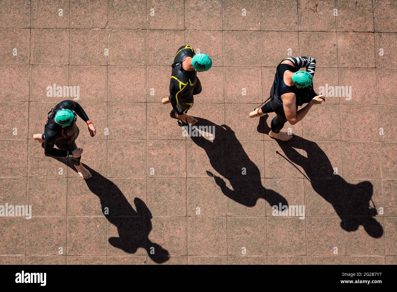 I triatleti del London Triathlon 2018 gettano lunghe ombre mentre camminano verso l'inizio della corsa di nuoto, Londra, Regno Unito Foto Stock