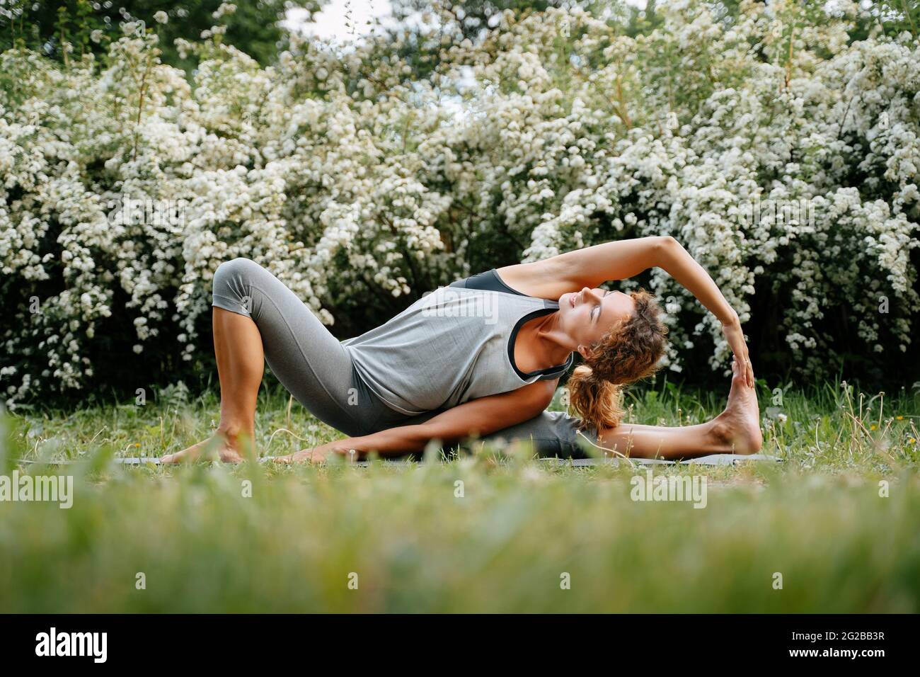 La sportiva pratica lo yoga sull'erba verde del parco. Foto Stock