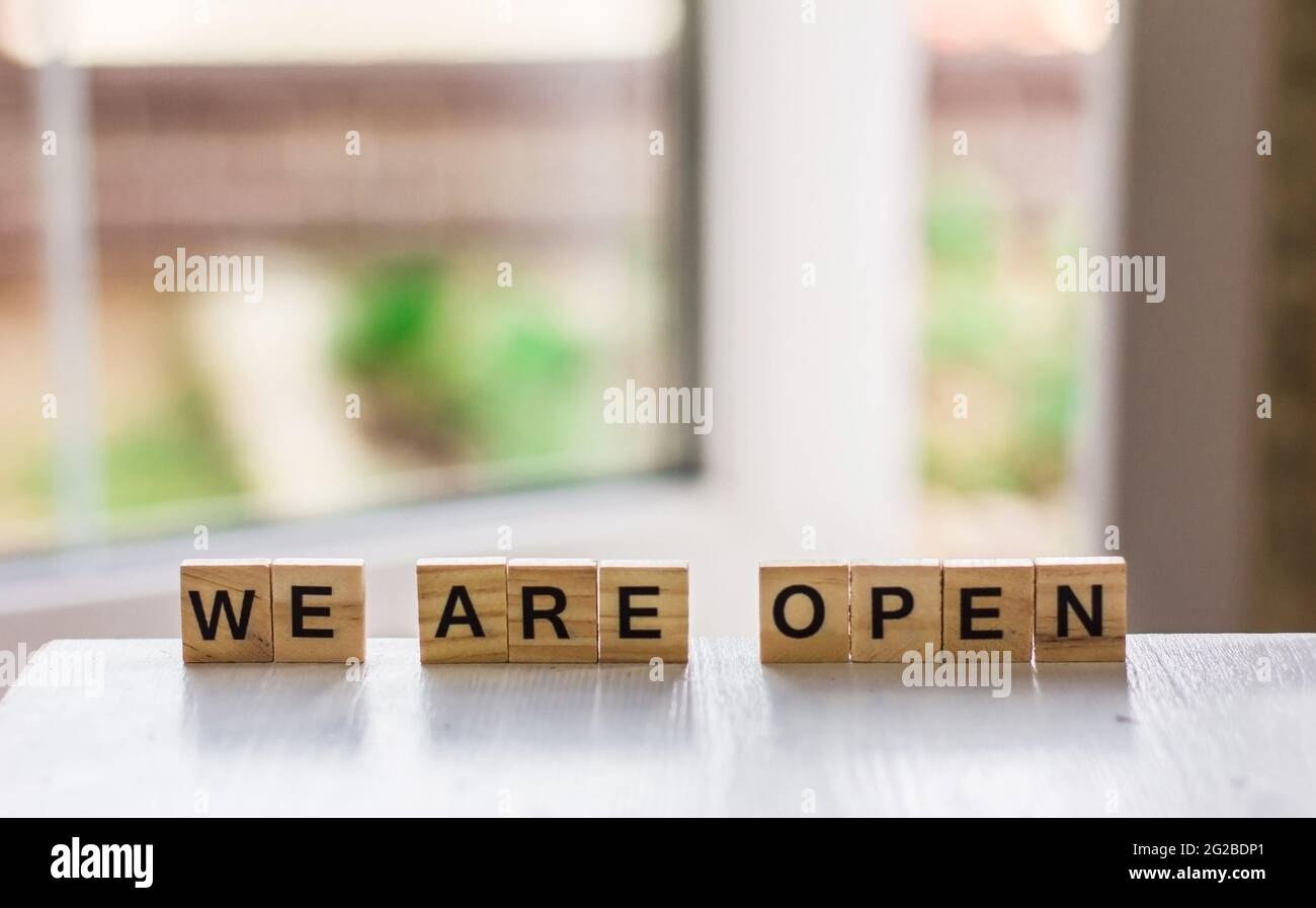 La parola 'siamo aperti' fatto di cubetti di legno sullo sfondo di una porta aperta, fine di quarantena un bar, un negozio locale, nel dare il benvenuto agli ospiti dopo il Foto Stock