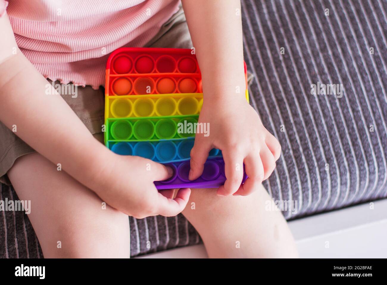 Una bambina si siede e tiene un giocattolo nelle sue mani arcobaleno pop esso fidget giocattolo. Premi bubble fidget sensoriale giocattolo in silicone stress rilievo giocattolo. Giocattolo antistress per Foto Stock