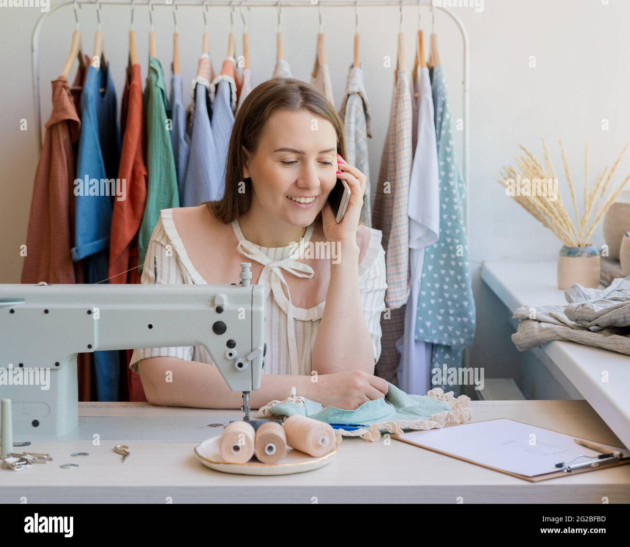 Buon marinaio che parla sul telefono cellulare mentre si siede sul suo posto di lavoro con la macchina da cucire in studio Foto Stock